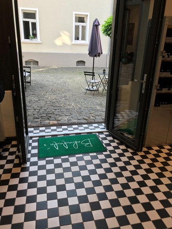 Blick durch geöffnete Tür auf Innenhof mit Sitzgruppe, Schachbrettfliesen und Fußmatte.