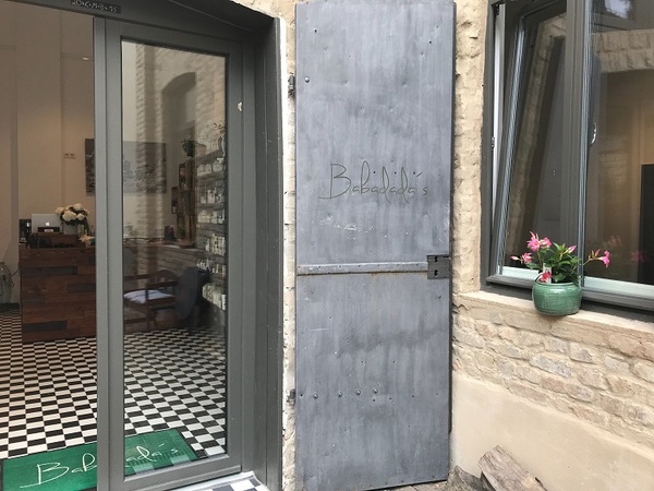 Eingang eines modernen Friseursalons mit Glasfront, dekorativen Fliesen und Pflanzen.