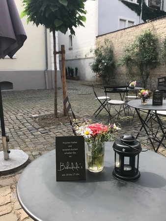 Gemütliches Café im Innenhof mit Blumen, Laterne und Tafel für Kaffee und Kuchen.