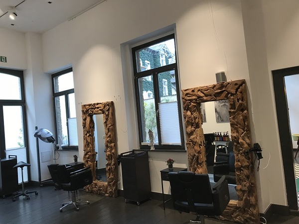 Moderner Friseursalon mit großen Spiegeln, Holzrahmen und stilvollen Friseurstühlen.