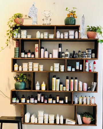 Holzregal mit vielen Kosmetikprodukten und Pflanzen als dekorative Elemente an der Wand.