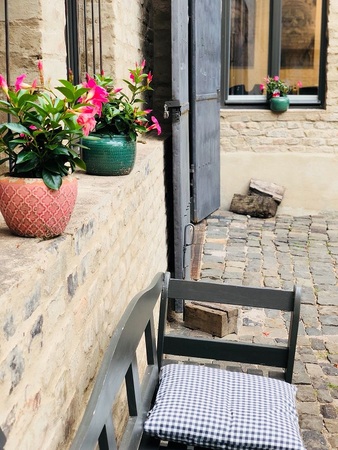 Gemütlicher Innenhof mit Pflastersteinen, Bank, Blumentöpfen und blühenden pinken Blumen.